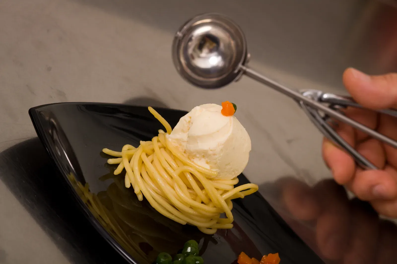 Gastronomic tuna and onion gelato served with spaghetti on a black plate.